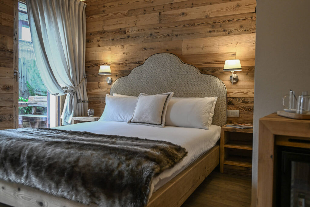 letto matrimoniale classico con parete in legno alle sue spalle in camera deluxe Stua Ceira al Baitin